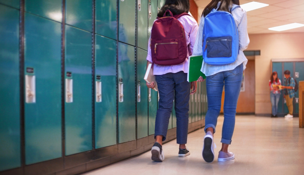 Two girls with backpacks walking on school hallway